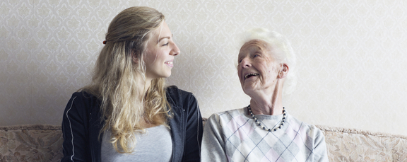 Enkelin und Oma sitzen auf Bank und lachen sich gegenseitig an