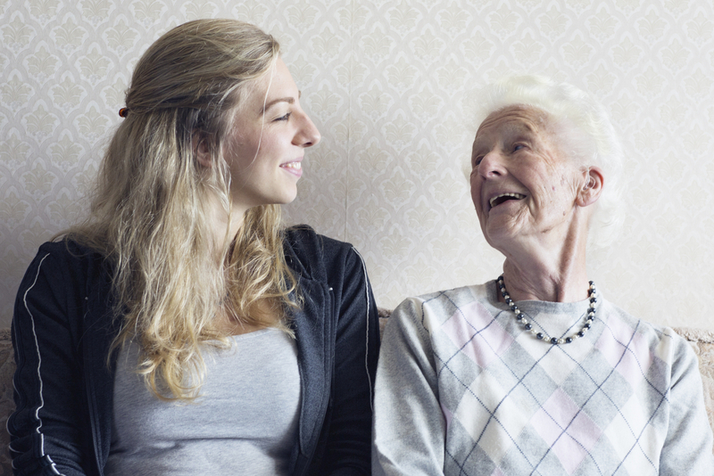 Enkelin und Oma sitzen auf Bank und lachen sich gegenseitig an