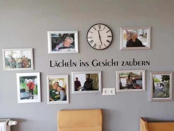 Wand mit Uhr und Fotos von Bewohner:innen des Pflegekompetenzzentrums Draßburg 