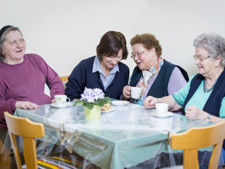 Drei Bewohnerinnen eines Pflegekompetenzzentrums beim Kaffeetrinken mit Betreuerin