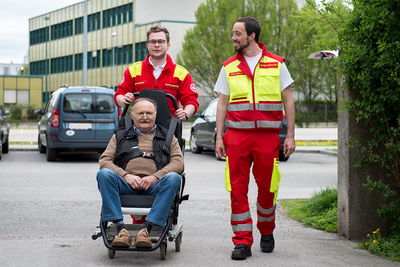 2 Samariter mit Patienten im Tragsessel auf Parkplatz