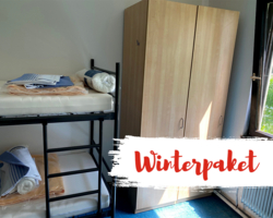 Innenaufnahme Winternotquariter, Stockbett aus schwarzem Stahl mit Bettwäsche, Polster, Decke, daneben Kasten, auf Bild Swusch mit roter Schrift: Winterpaket