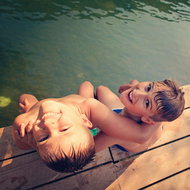 2 Kinder sitzen auf Holzsteg über einem Teich