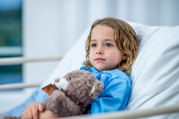 Kind im Krankenhausbett mit Teddybär