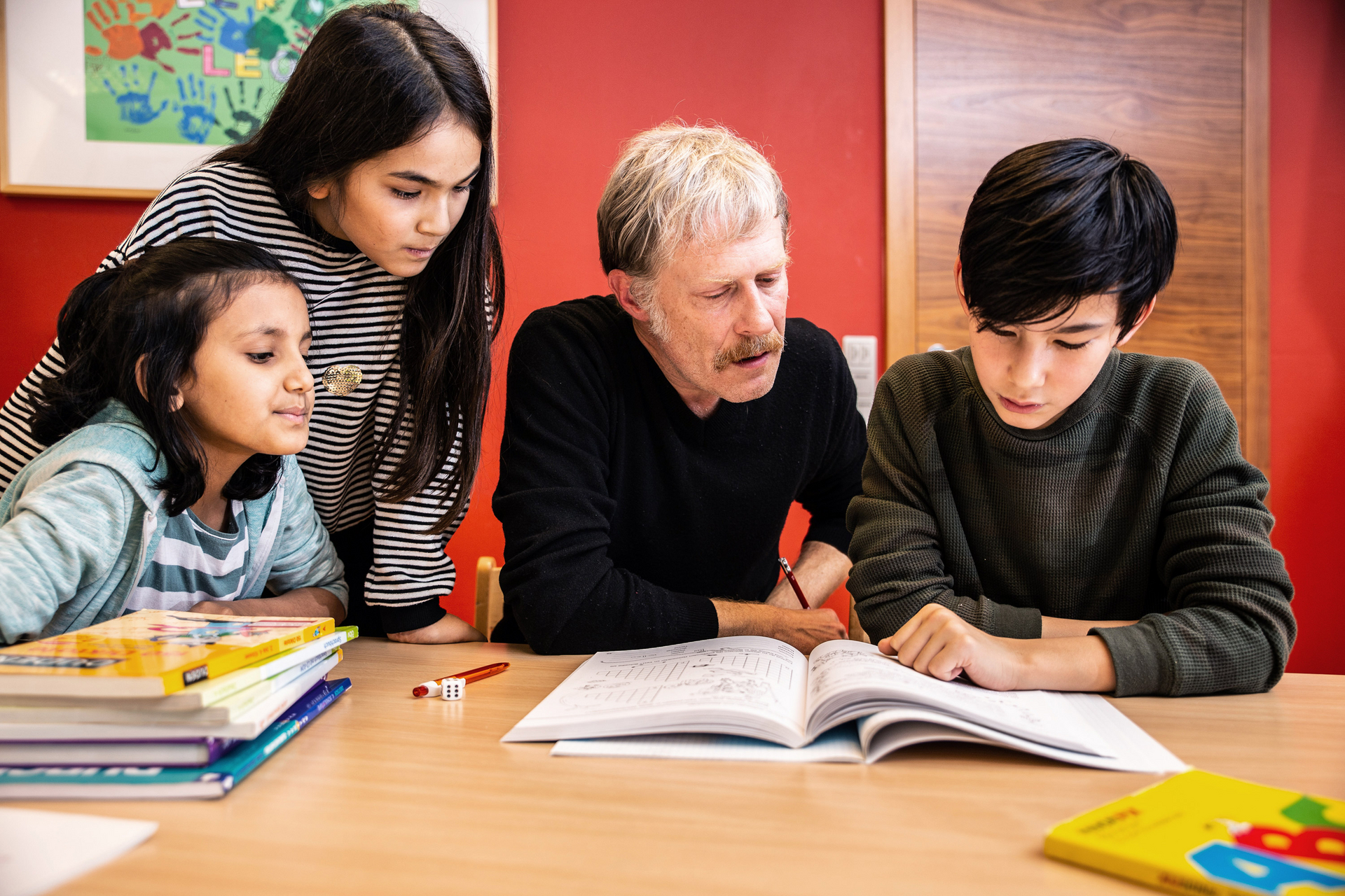 Lehrer gibt mehren Kindern Nachhilfe und sie schauen gemeinsam in ein Buch.