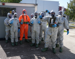 Gruppe von Personen im Schutzanzug schaut in die Kamera für Gruppenbild, Geräte für Strahlungsdetektion in der Hand, Atemschutzmasken