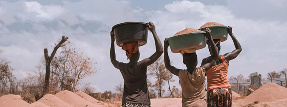 Drei Afrikanerinnen tragen Plastikbehälter, gefüllt mit Erde, auf dem Kopf