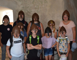 Mehrere Kinder stehen in einer Burg und haben mitteralterliche Helme auf.