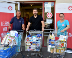 drei Personen vor Sozialmarkt Eingang, drei volle Einkaufswagerl mit Waren, alle drei lächeln in Kamera