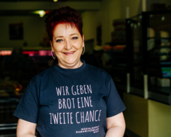 Frau mit kurzen rötlichen Haaren; T-Shirt mit Spruch Wir geben Brot eine zweite Chance, im Hintergrund SOMA