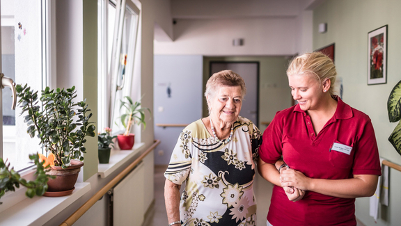 Altenpflegerin führt Bewohnerin eines Pflegekompetenzzentrums über den Gang