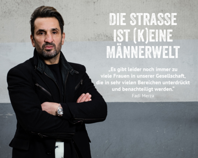 Fadi Merza vor grauer Wand, Porträt, dunkle Kleidung, verschränkte Hände, Slogan Die Straße ist (k)eine Männerwelt plus Zitat