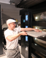 Bäcker in mel&koffie Filiale im neunten Bezirk, schiebt Blech in großen Backofen