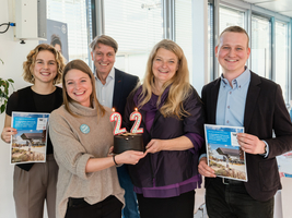 Auf dem Bild sind 3 Frauen und 2 Männer zu sehen. Zwei Personen in der Mitte halten eine Torte, die mit Kerzen verziert sind, die die Zahl 22 darstellen. Zwei Personen am Rand halten einen Folder von einer Studie der WU.