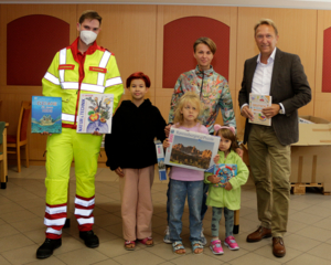 Gruppenfoto Kinder aus Haidehof, Geschäftsführer Morawa und Sanitäter in Uniform mit FFP2-Maske, halten Spielsachen in den Händen