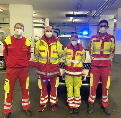 Sanitäterinnen mit Maske, in Uniform vor Rettungsauto, in einer Garage
