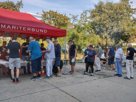 Aufnahme beim Sommerfest Haus Riga, mehrere Menschen stellen sich an um Essen bei Samariter Suppentopf zu holen 