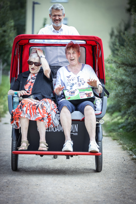 zwei ältere Damen sitzen in einer Rikscha und lachen, werden gefahren von Samariterbund Wien Geschäftsführer Oliver Löhlein
