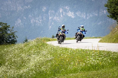 Zwei Polizeimotorräder fahren auf einer kurvenreichen Straße in der Natur.